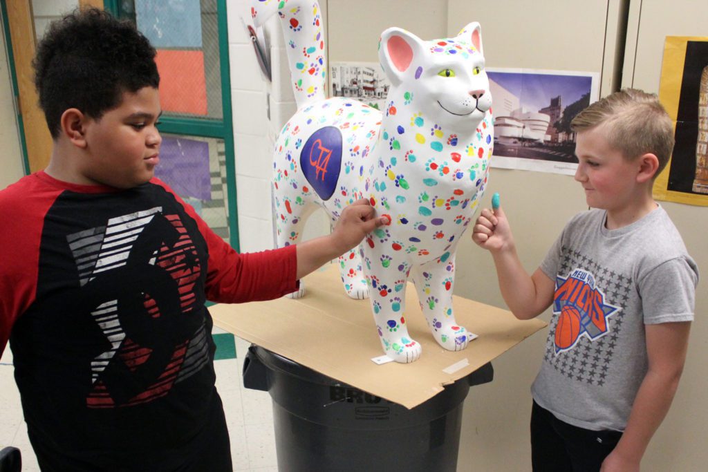 students stamp thumbprints onto cat statue