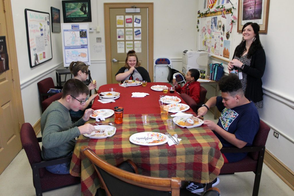 students eating meal at table while being served by teachers.