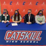 two girls, woman, and man sitting at table with Catskill High Banner on it, wearing masks