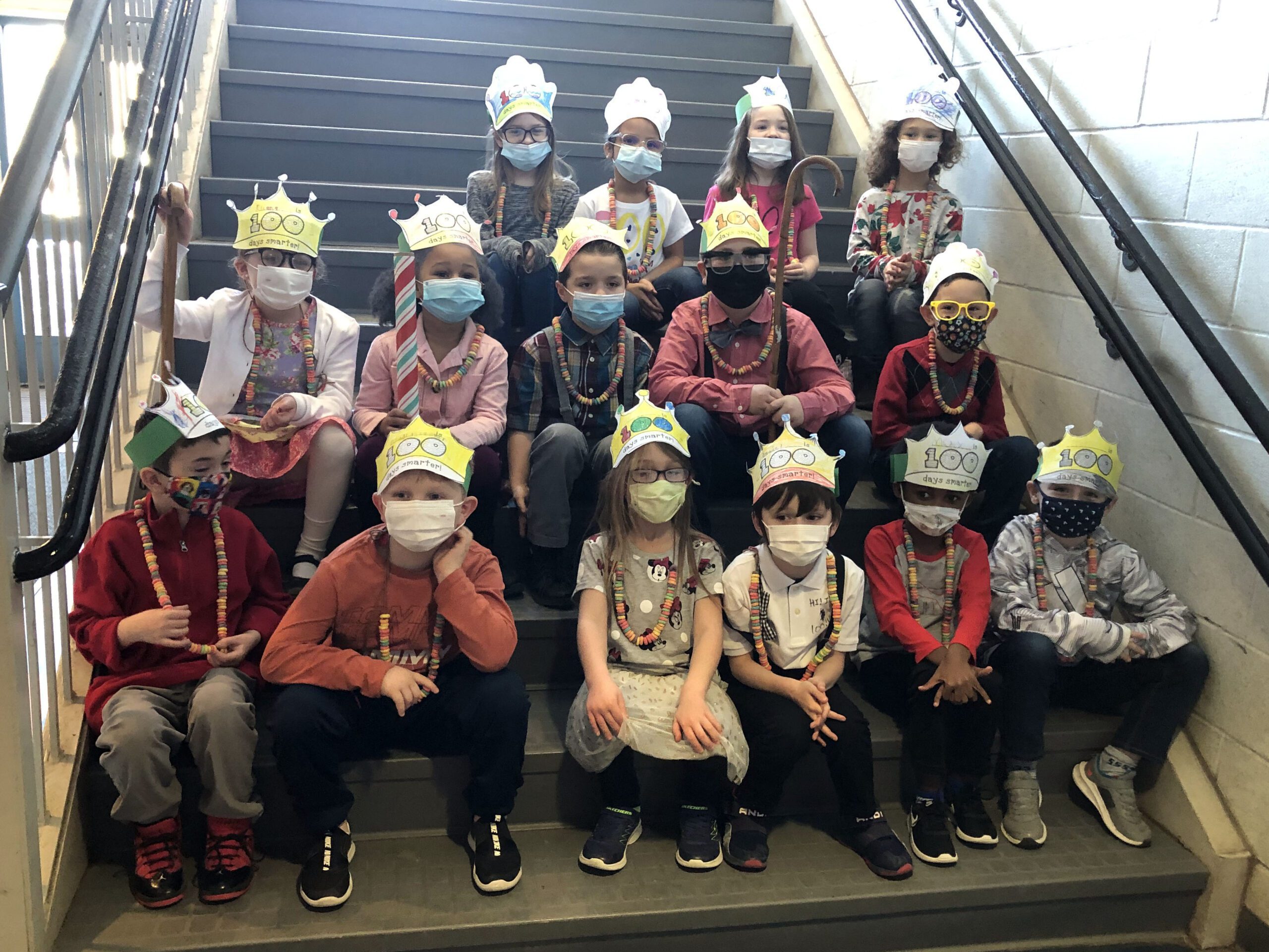 first grade class poses on stairs dressed as old people and wearing bead necklaces 