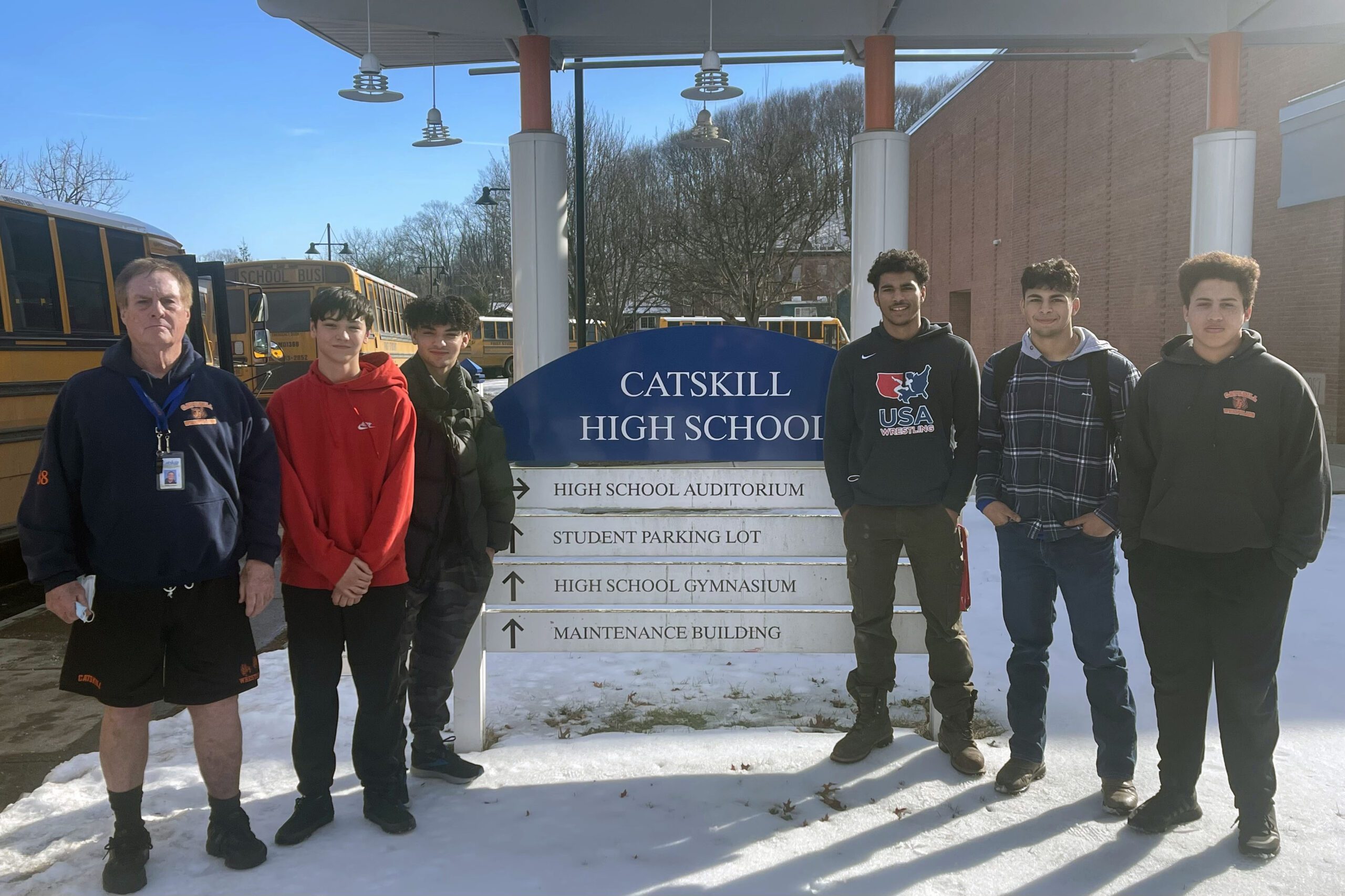 Coach and five wrestlers pose by sign