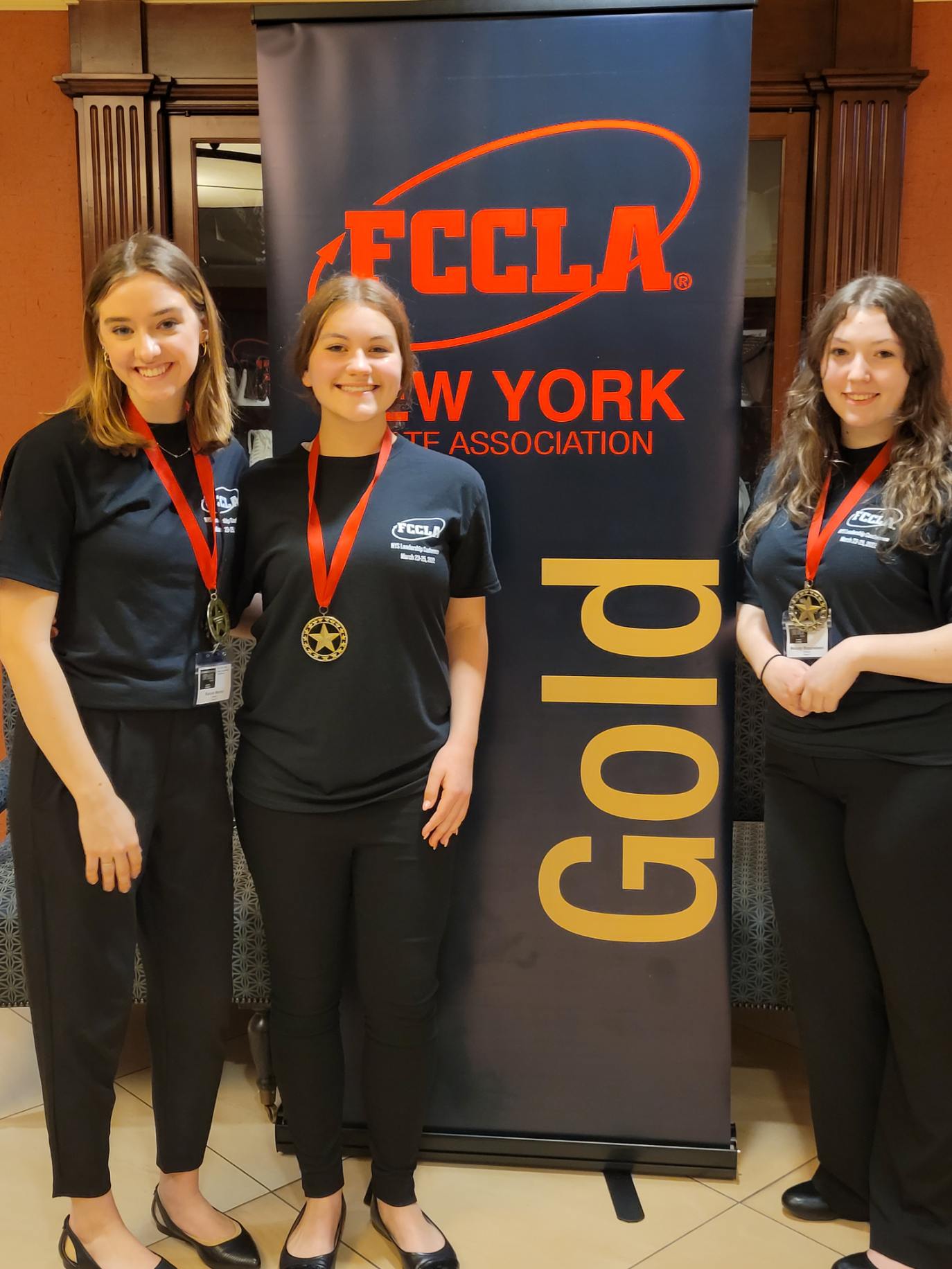 thre girls standing next to gold award sign