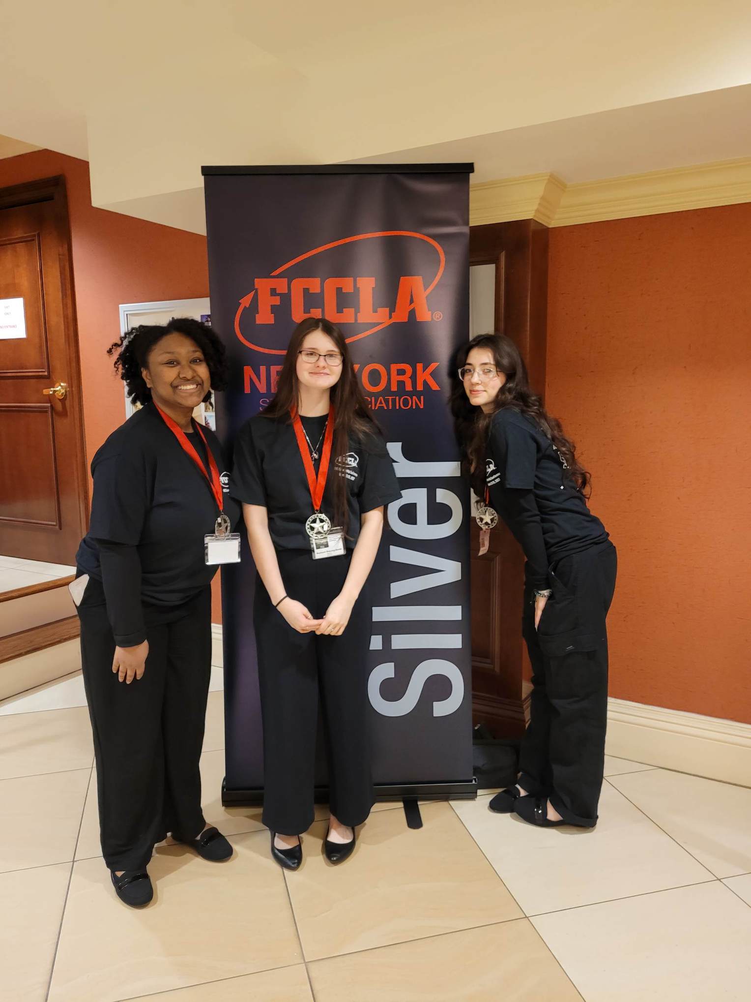 three girls standing next to silver award sign