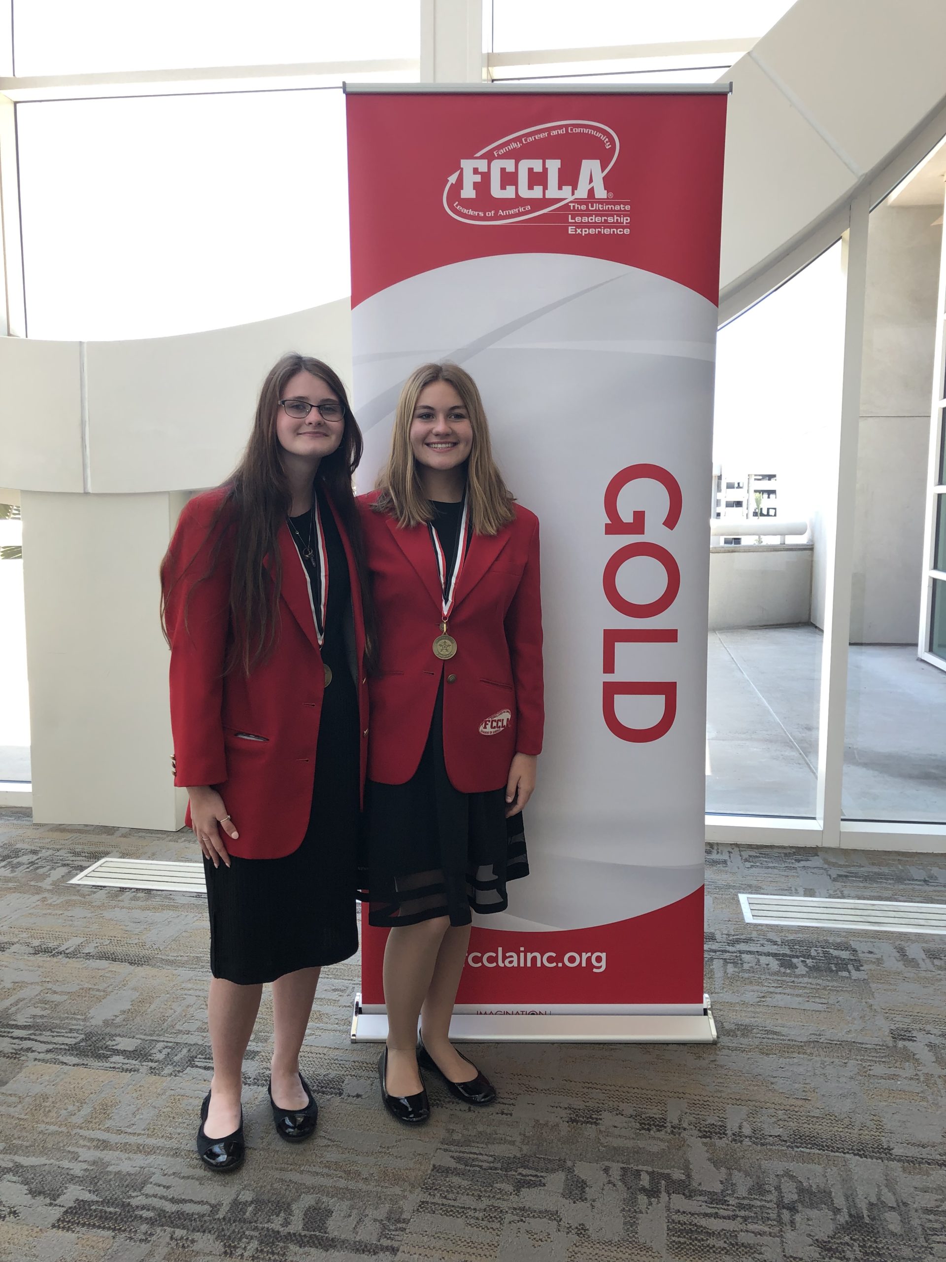 two girls pose by gold winners sign