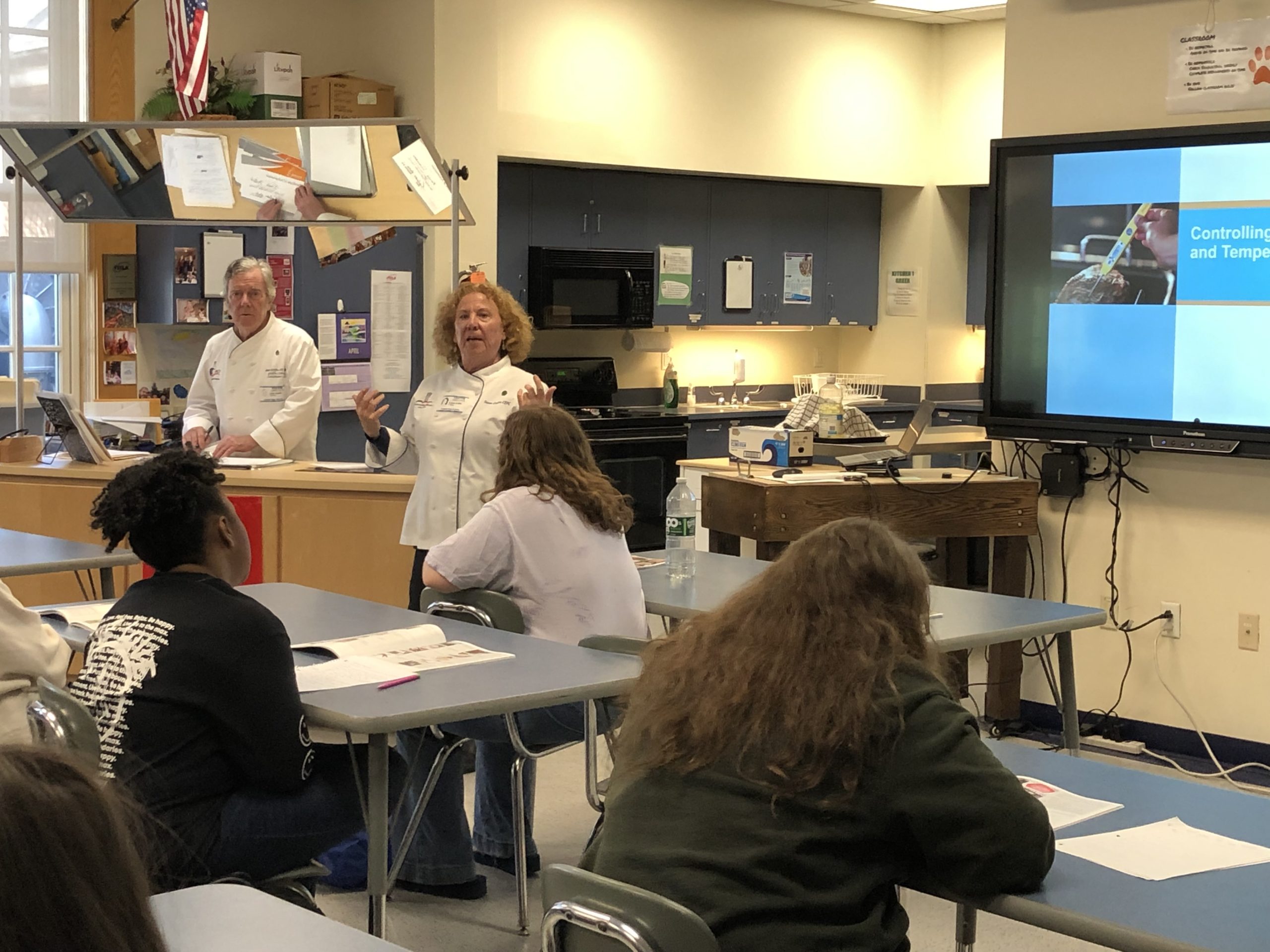 man an woman in chef's coats talking to class