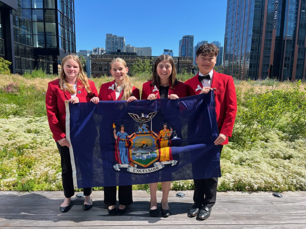four students in FCCLA uniforms holding NYS flag