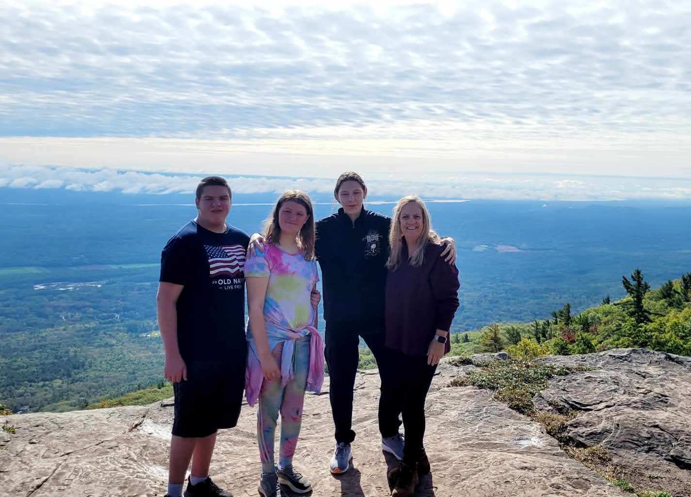studentsand staff standing on top of mountain with wide-spanning view behind them.