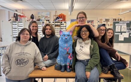 group of high school age students pose with painted cat sculpture