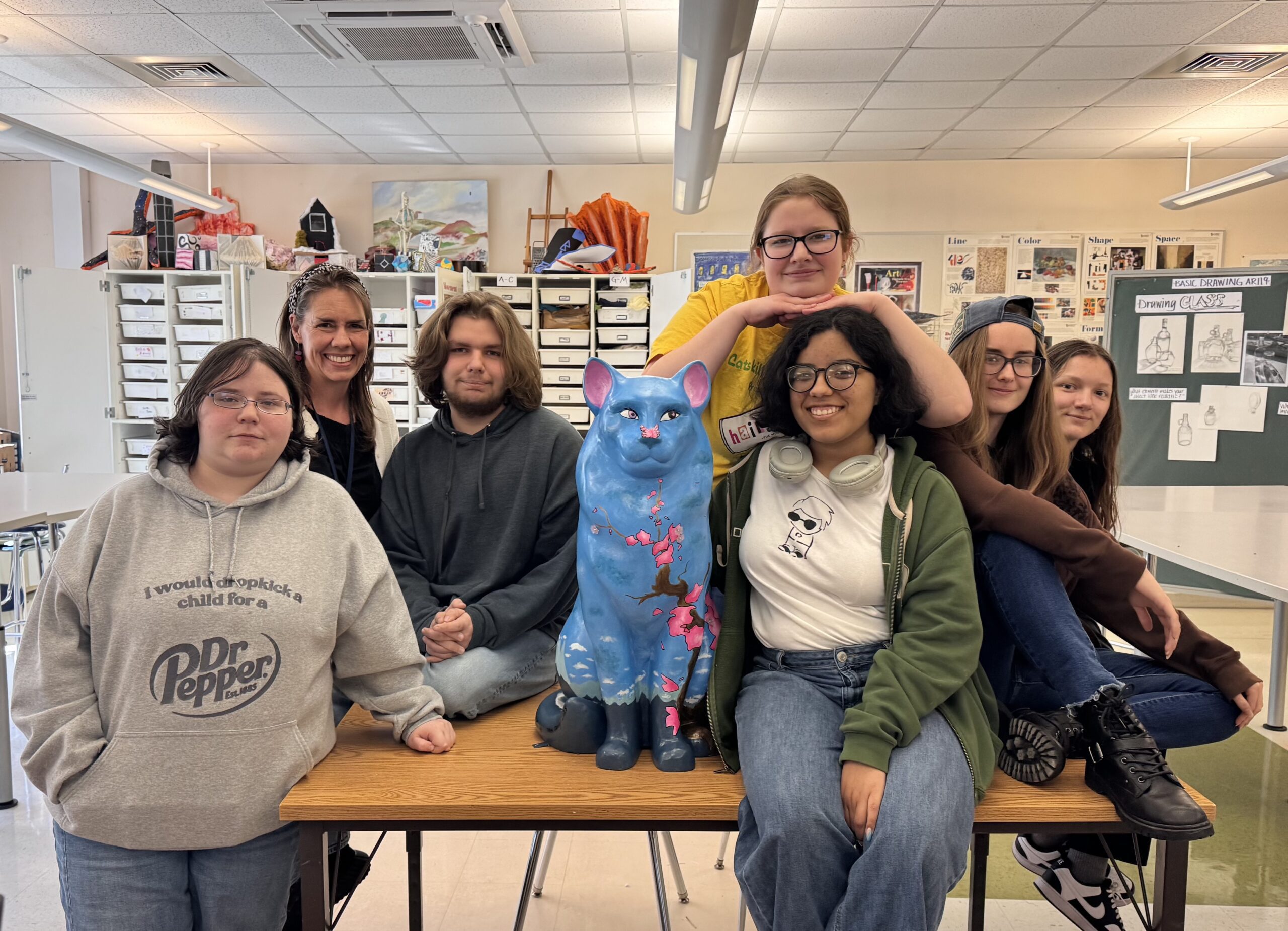 group of high school age students pose with painted cat sculpture
