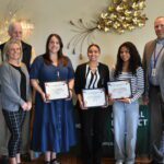woman and two teenage girls holding certificates flanked by woman and two men