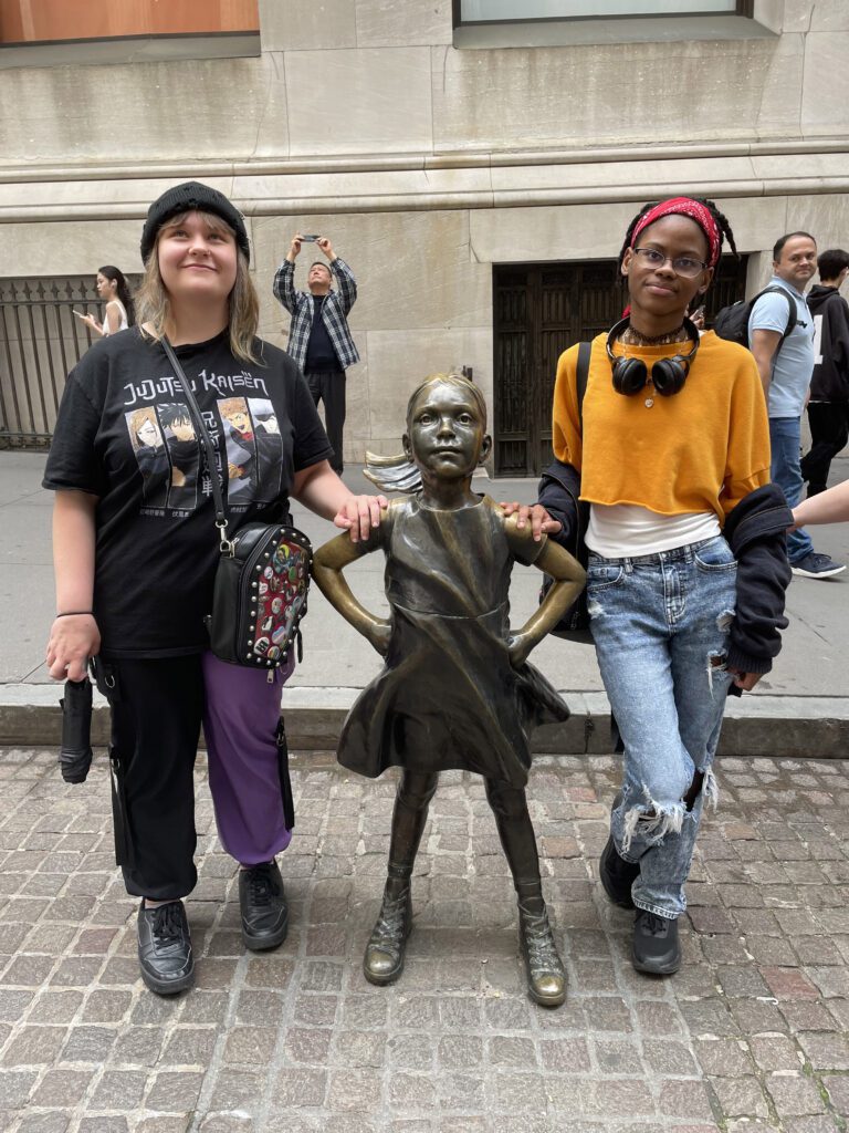 two girls pose with Fearless Girl statue