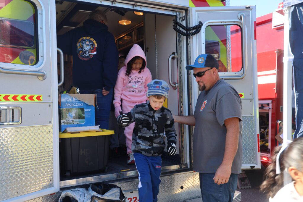 boy and girl stepping out of firetruck with help from fireman