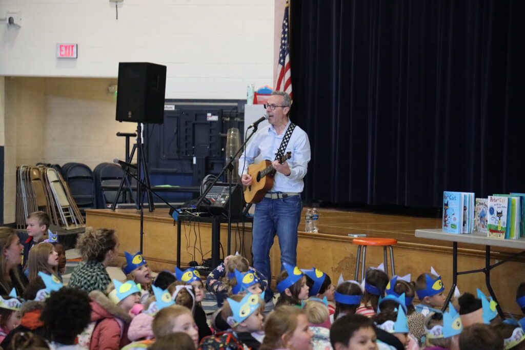 man playing guitar in front of crowd of young students