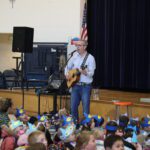 man playing guitar in front of crowd of young students
