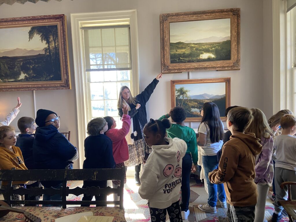 woman pointing to painting on wall in front of a group of students