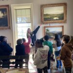woman pointing to painting on wall in front of a group of students