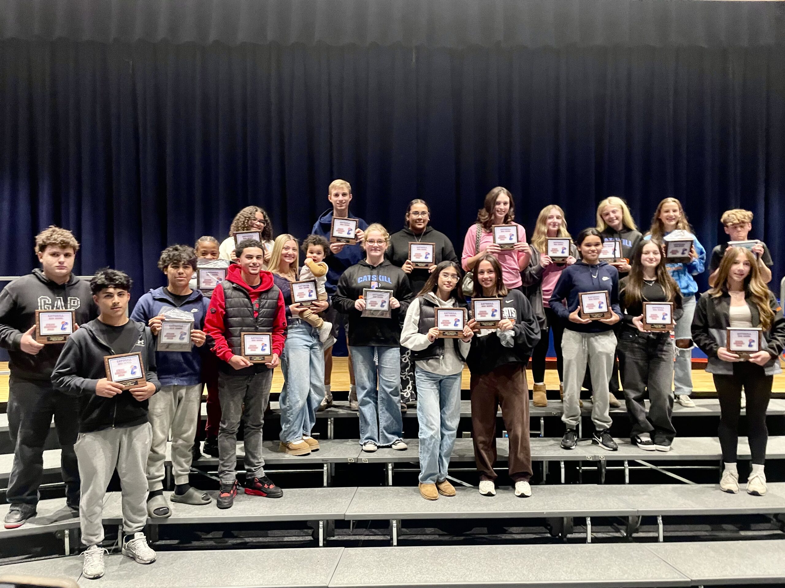 2025 Fall Sports Awardees standing on bleachers holding certificates