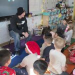 young man speaking to classroom of second graders seated on the floor