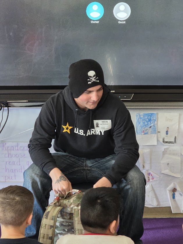 young man siting in chair and showing students Army backpack