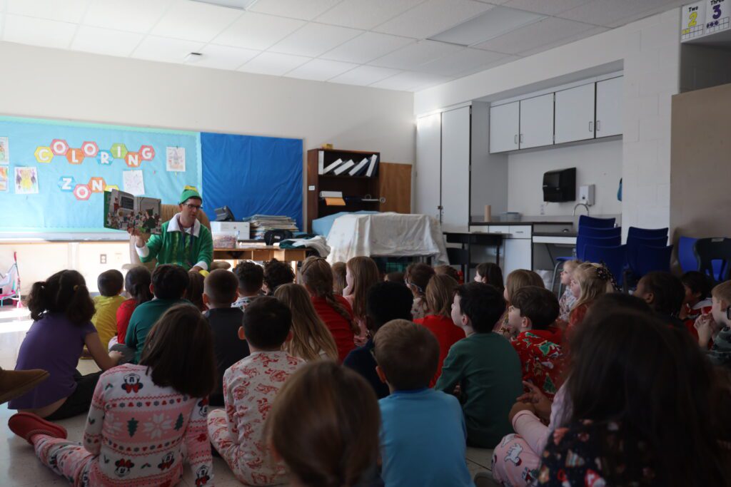 Man dressed as Buddy the Elf reading to classroom of students