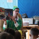 Man dressed as Buddy the Elf reading to classroom of students