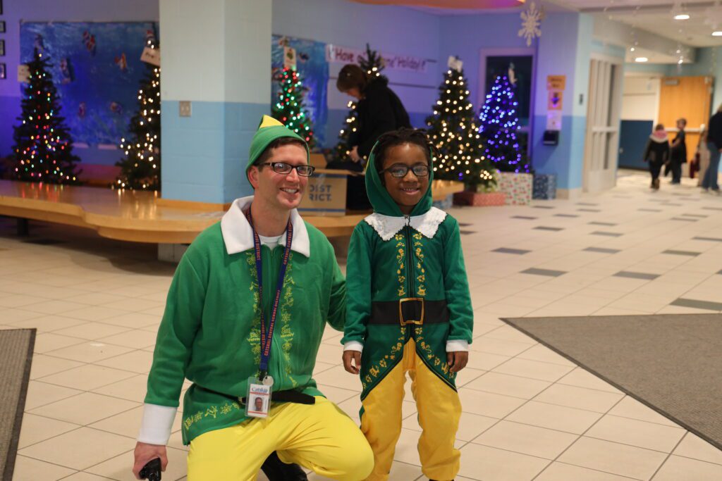 Man dressed as Buddy the Elf posing with smiling boy in school hallway