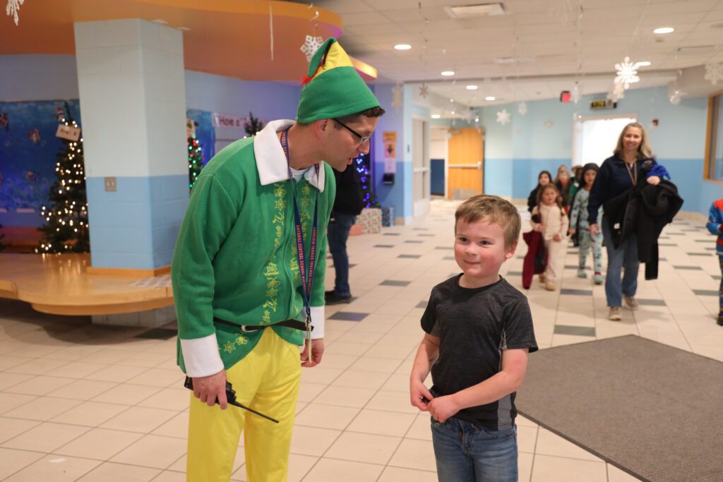Man dressed as Buddy the Elf talking to smiling boy in school hallway