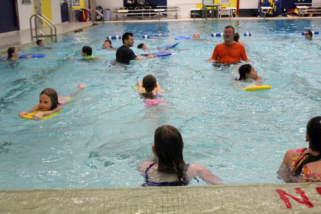 students swimming while being instructed by two men.