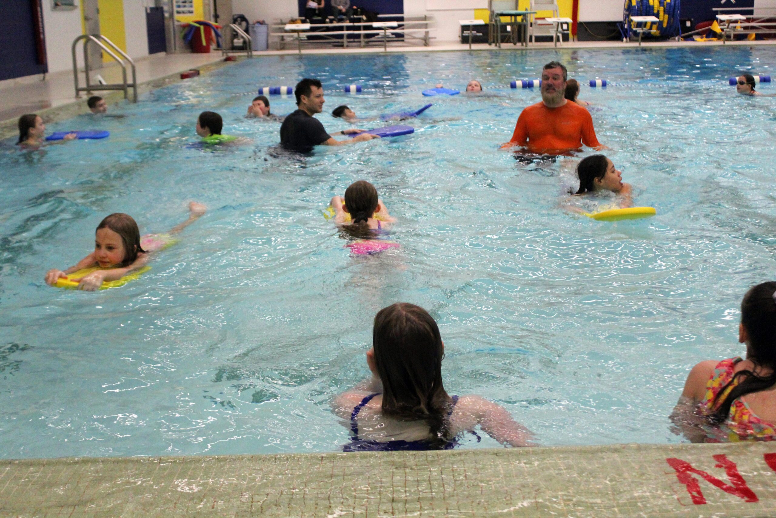 students swimming while being instructed by two men.