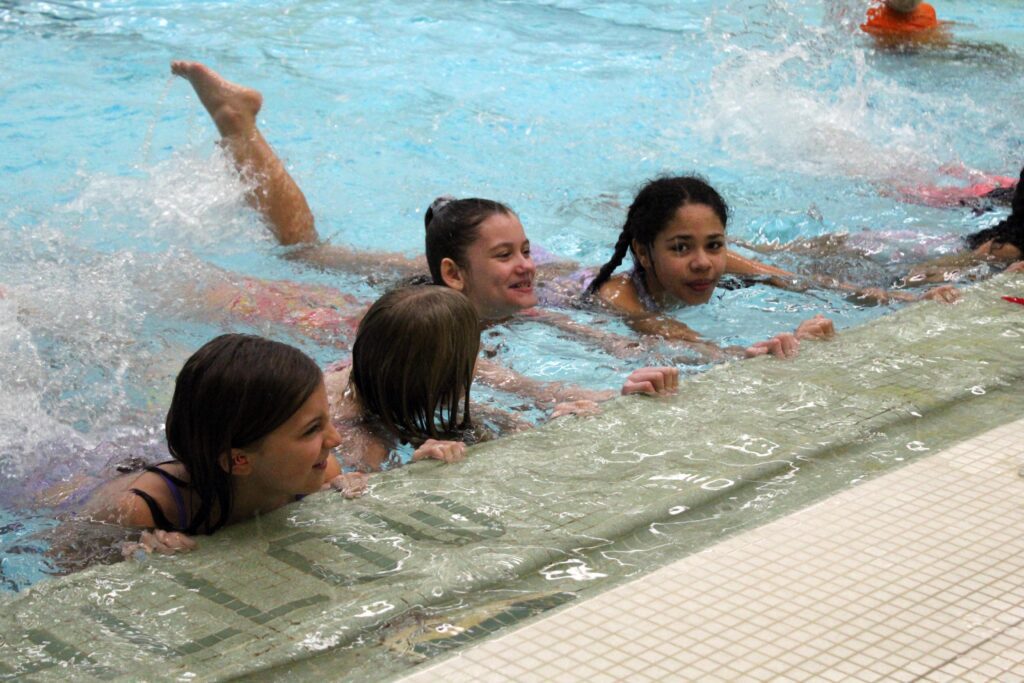 students practicing swim kicks along pool wall