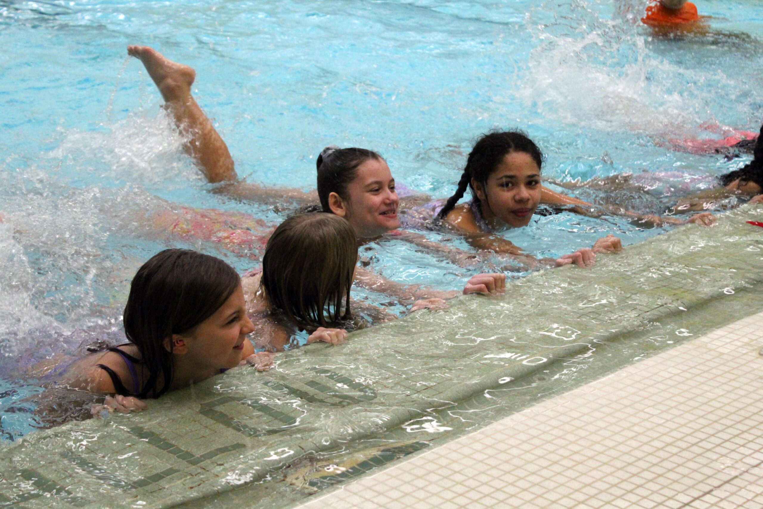 students practicing swim kicks along pool wall
