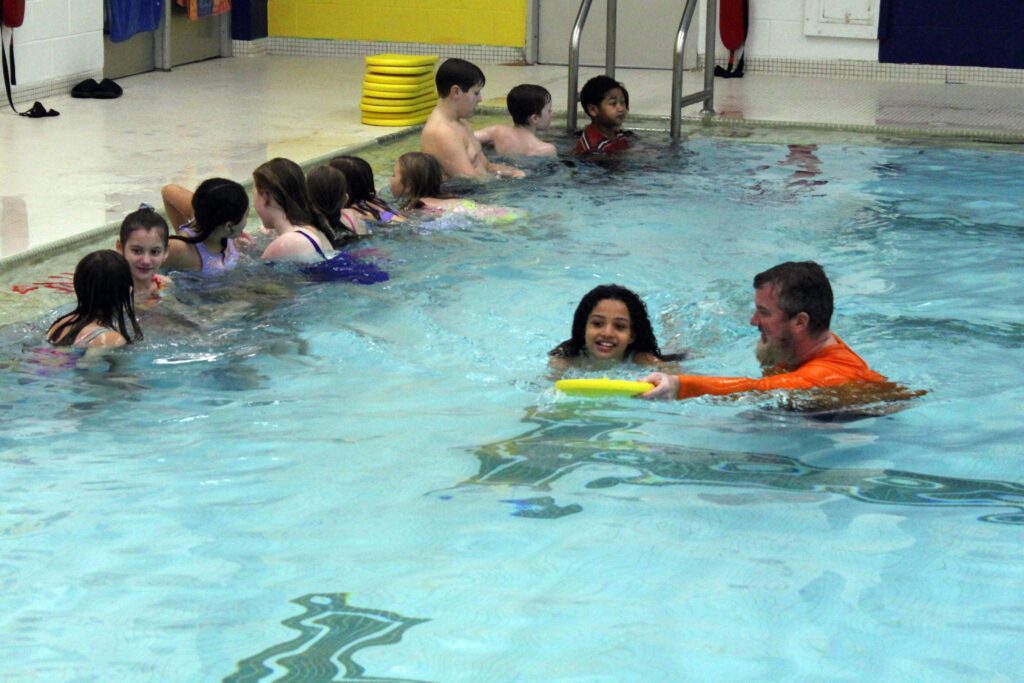 girl swimming with kickboard being instructed by man
