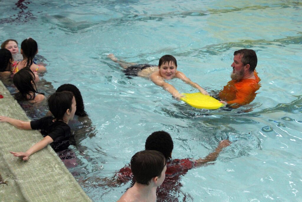 boy swimming with kickboard being instructed by man