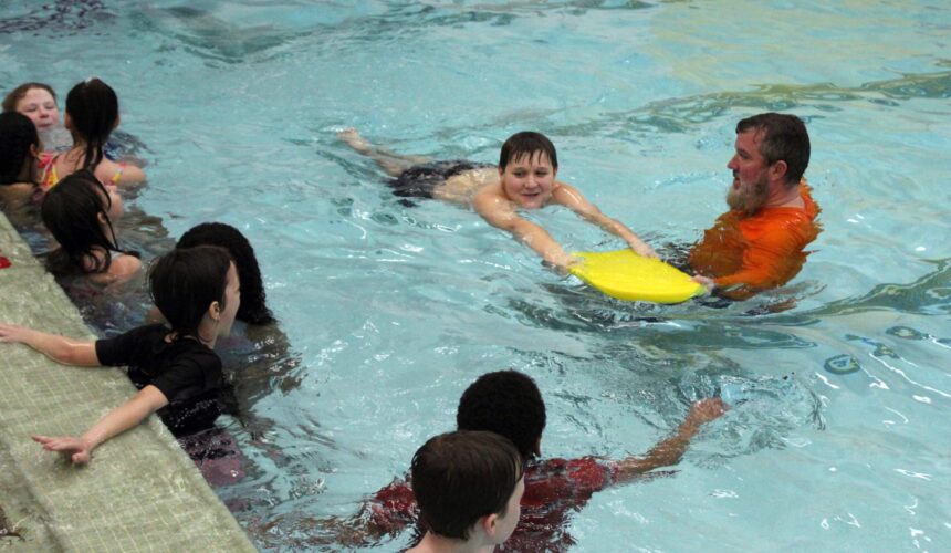 boy swimming with kickboard being instructed by man