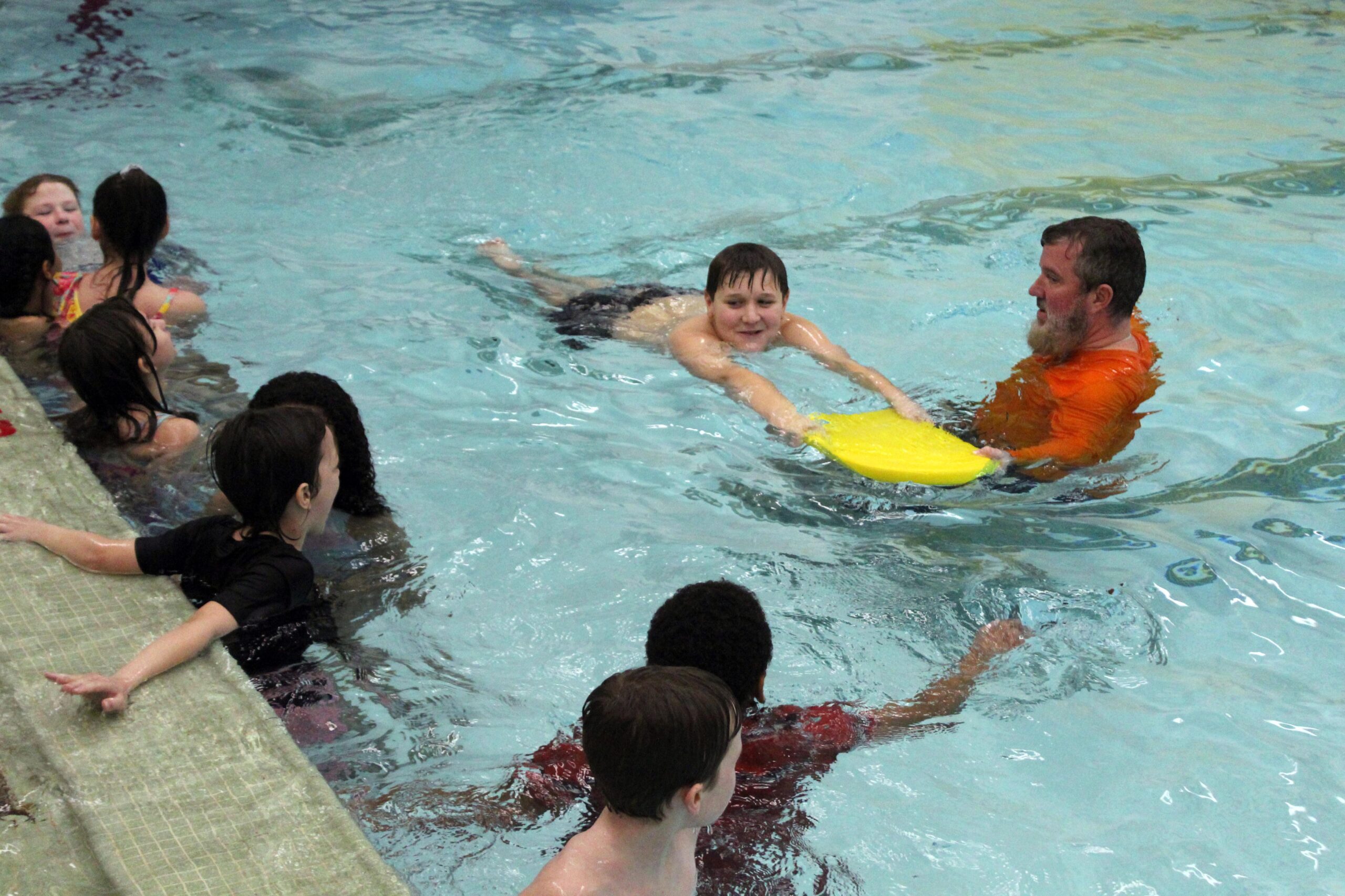 boy swimming with kickboard being instructed by man