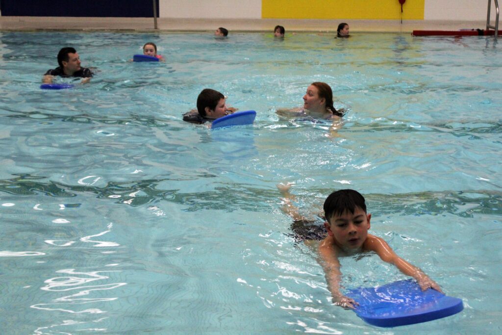 students swimming with kickboards being instructed by man and woman