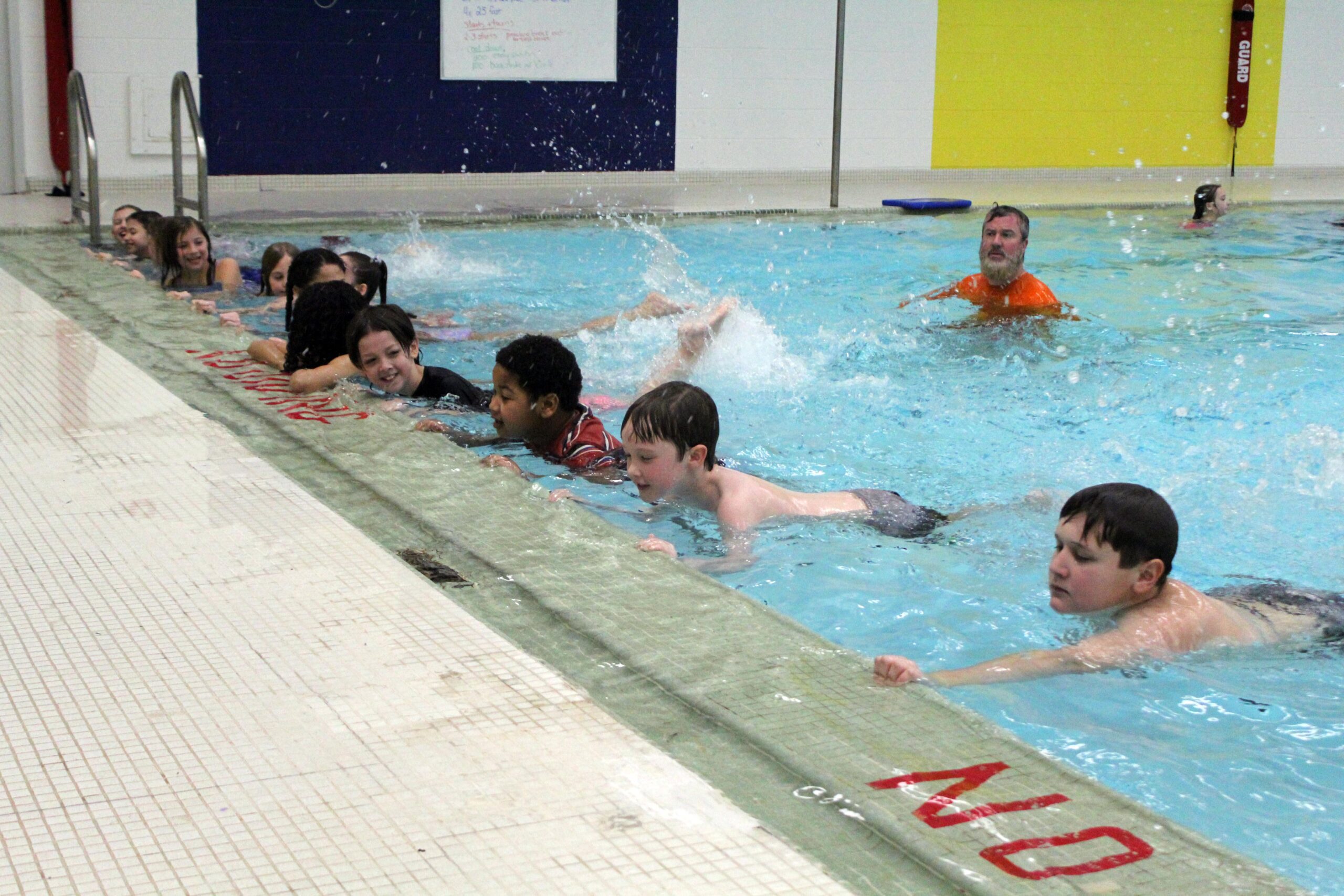 students practicing swim kicks along pool wall