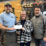 two men and woman pose with check in bike shop