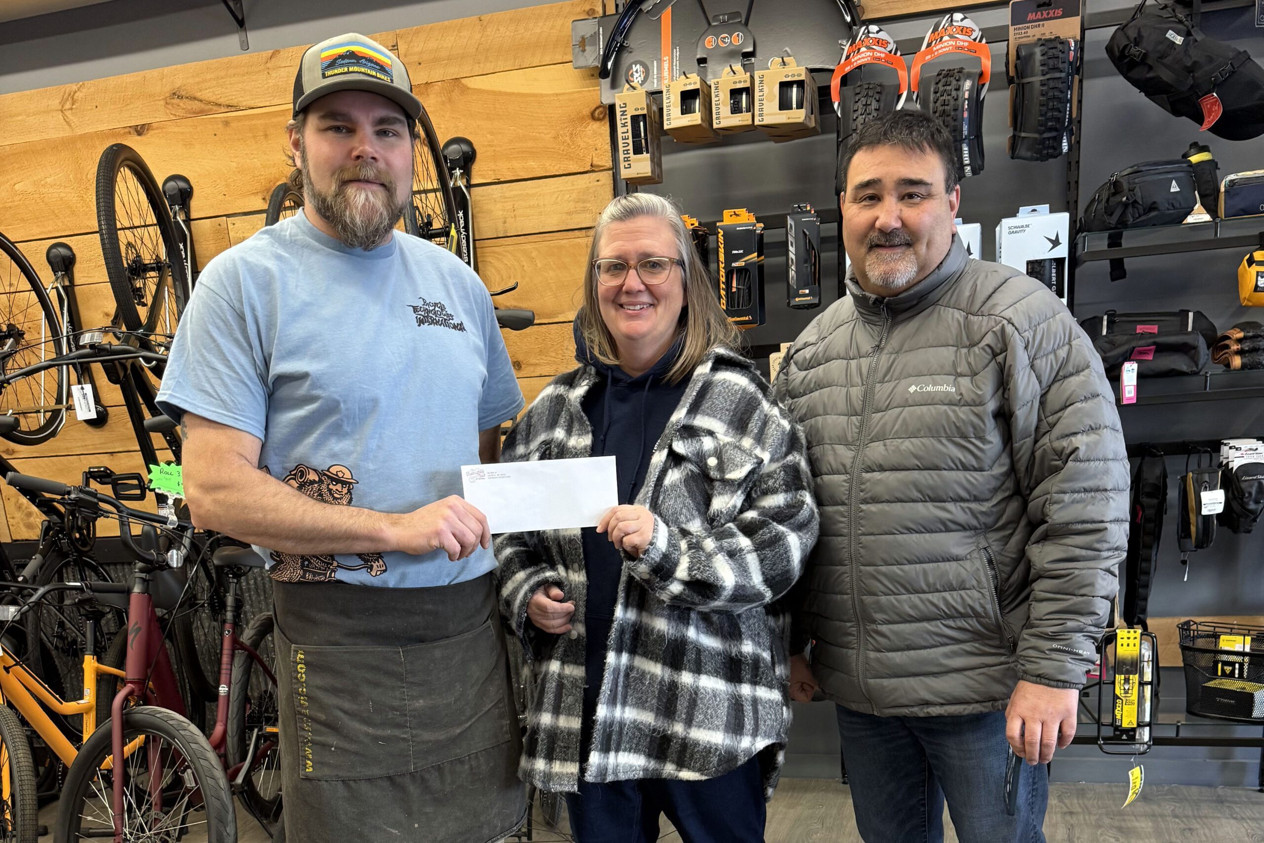 two men and woman pose with check in bike shop