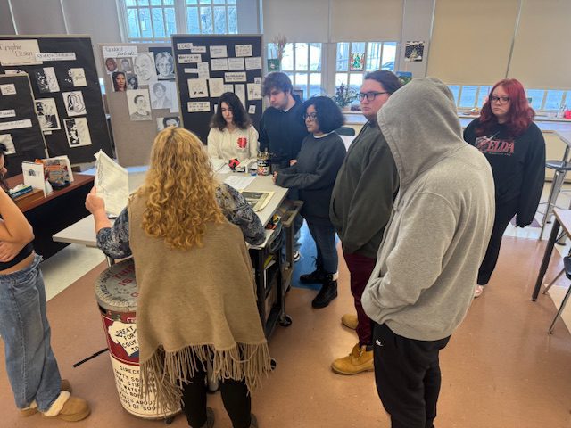 woman showing students art on classroom table