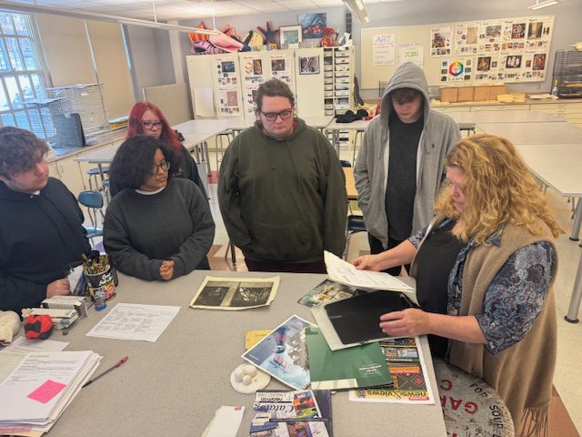 woman showing students art on classroom table