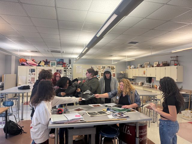 woman showing students art on classroom table