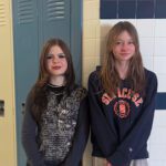 Two girls smiling in front of hallway lockers