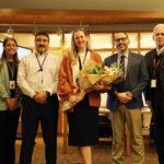 woman holding flowers flanked by school administrators