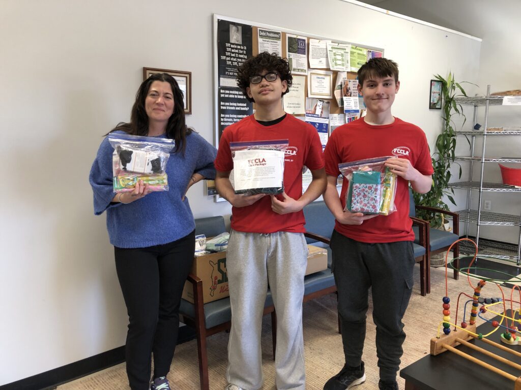 two young men presenting woman with care packages.