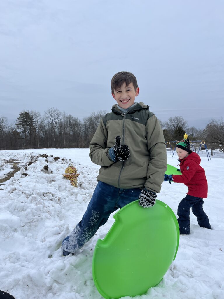 boy giving thumbs up and holding sled