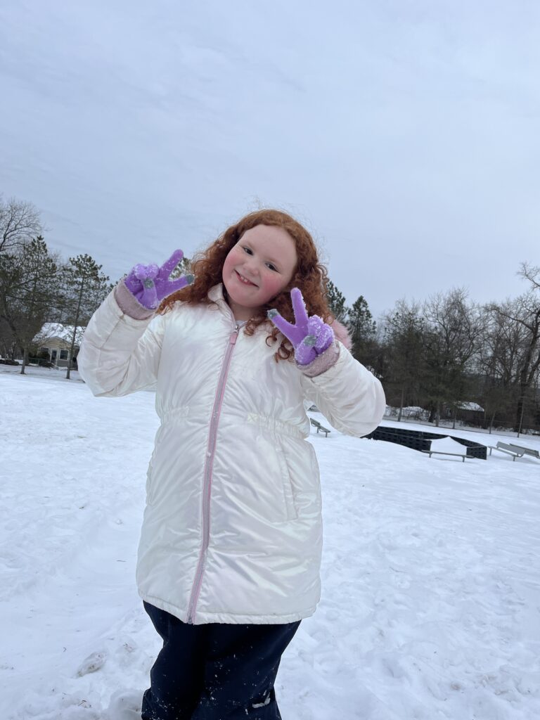 girl making peace sign while standing out side in snow