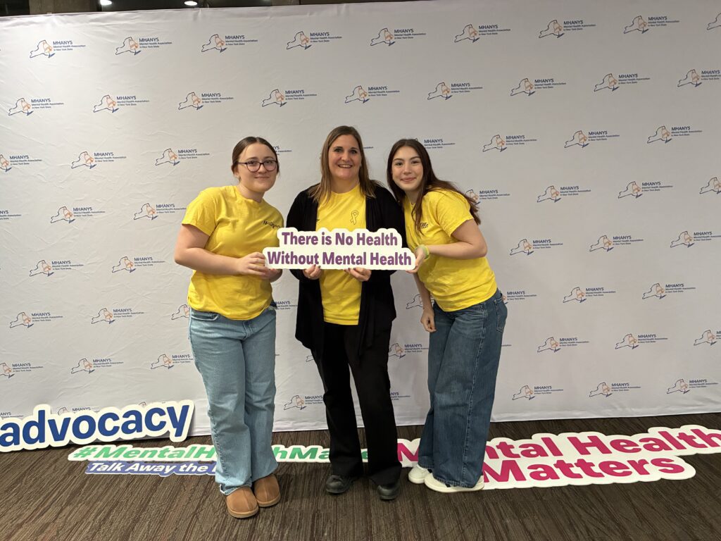 two students and woman holding sign that says there is no health without mental health