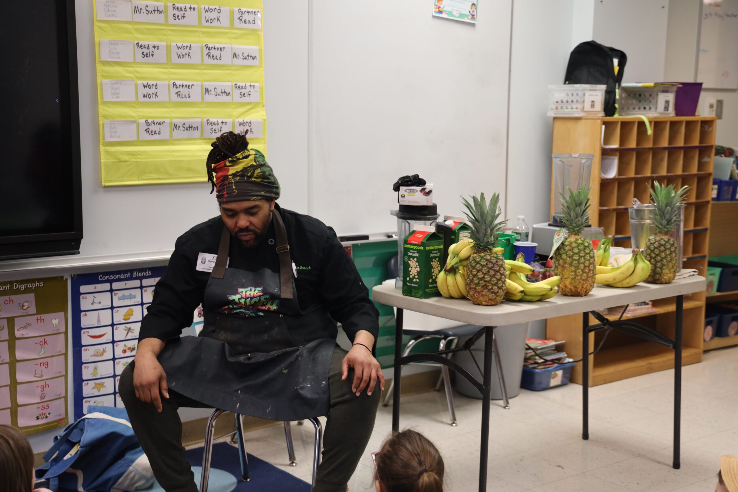 man seated next to tropical fruit ion table giving job presentation in classroom