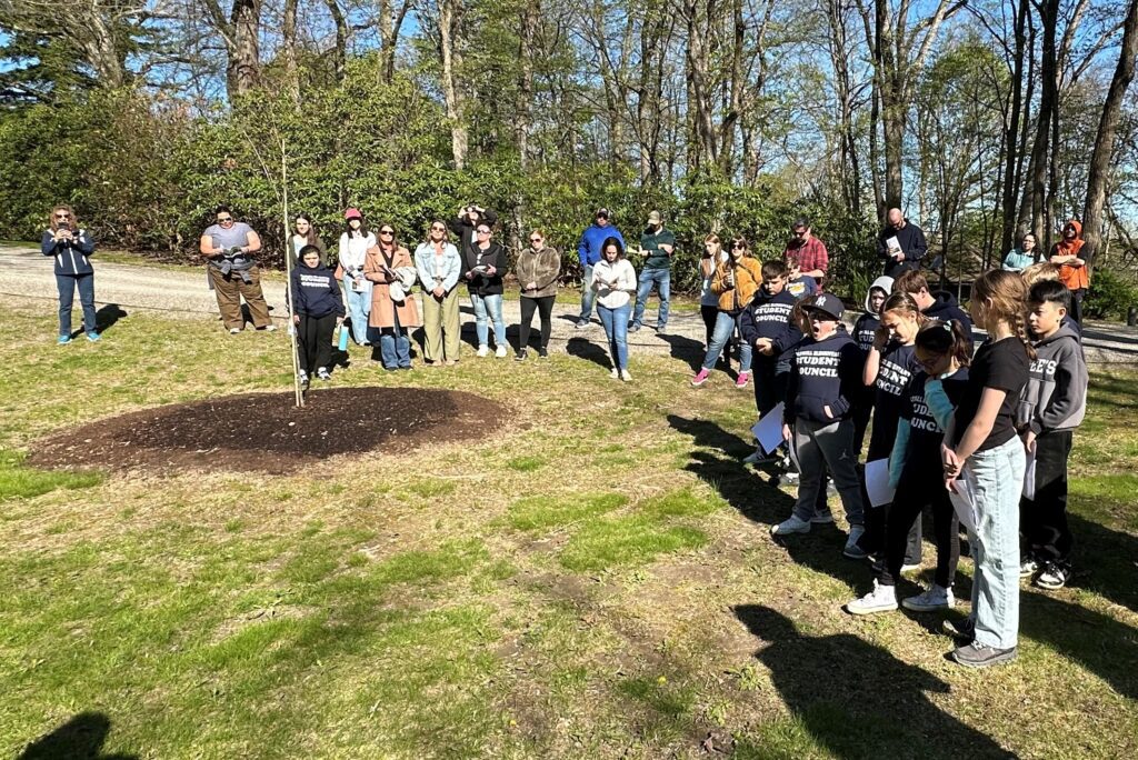 large group of people gathered around a recently planted tree.